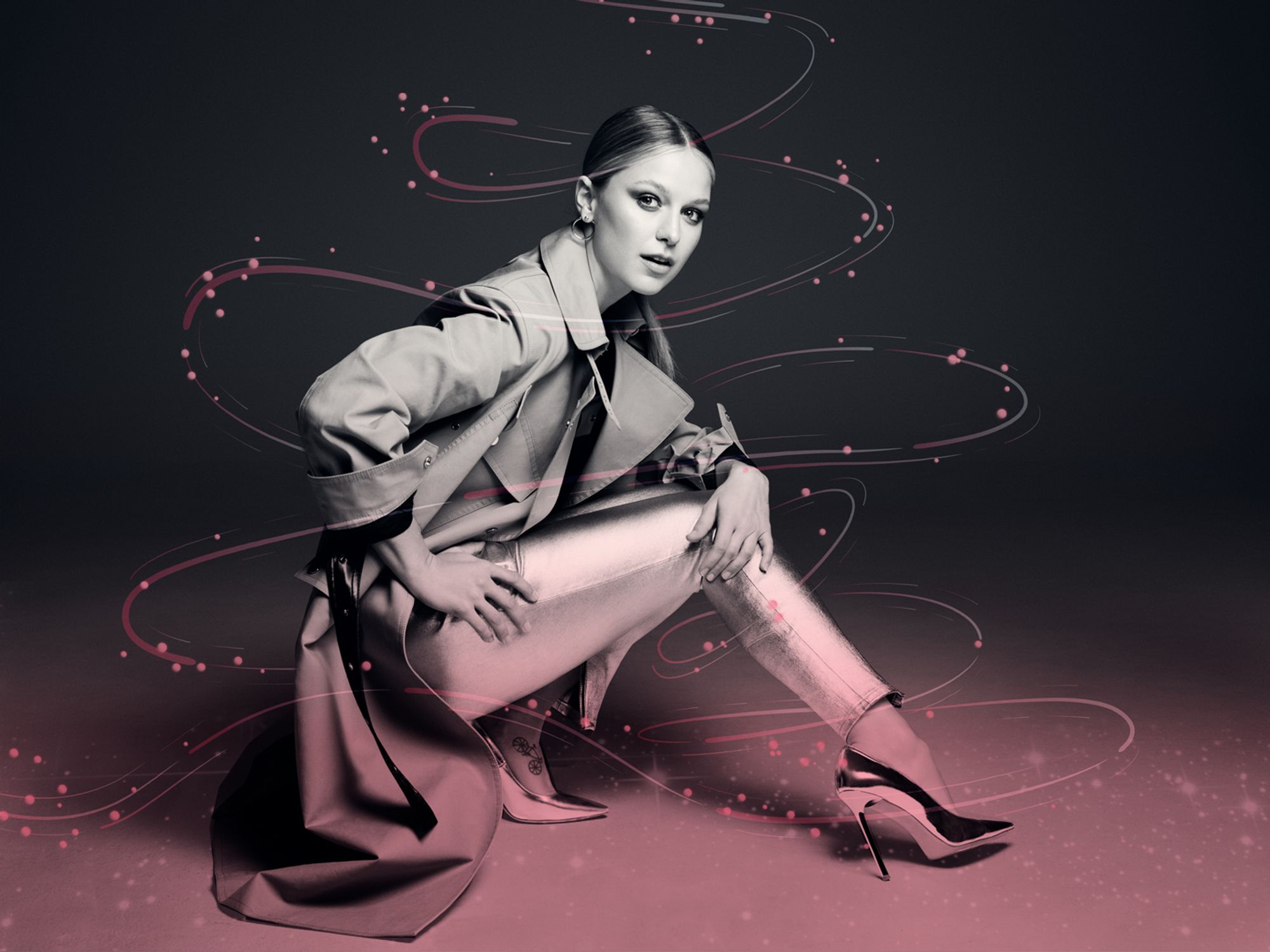 Supergirl Star Melissa Benoist wears a trench coat and shiny pants and shoes.