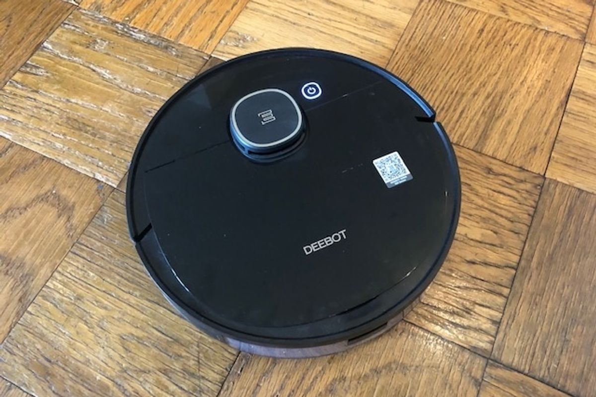 Round, black robot vacuum with the word "DEEBOT" on top on a wood floor