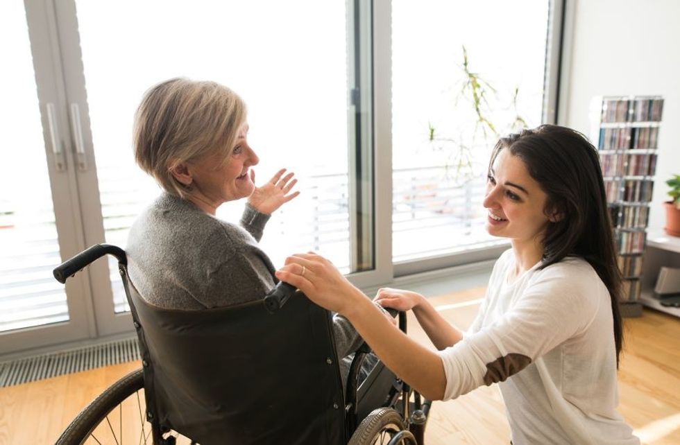 Personal care aide taking care of a wheelchair-bound patient in their home.