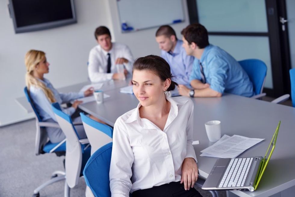Woman office worker looking lonely and sitting separate from her co-workers at a meeting.
