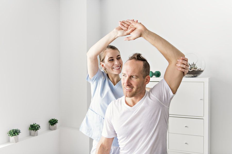 Occupational therapy assistant helping a patient stretch in a doctor's office.