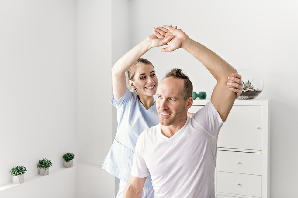 Occupational therapy assistant helping a patient stretch in a doctor's office.