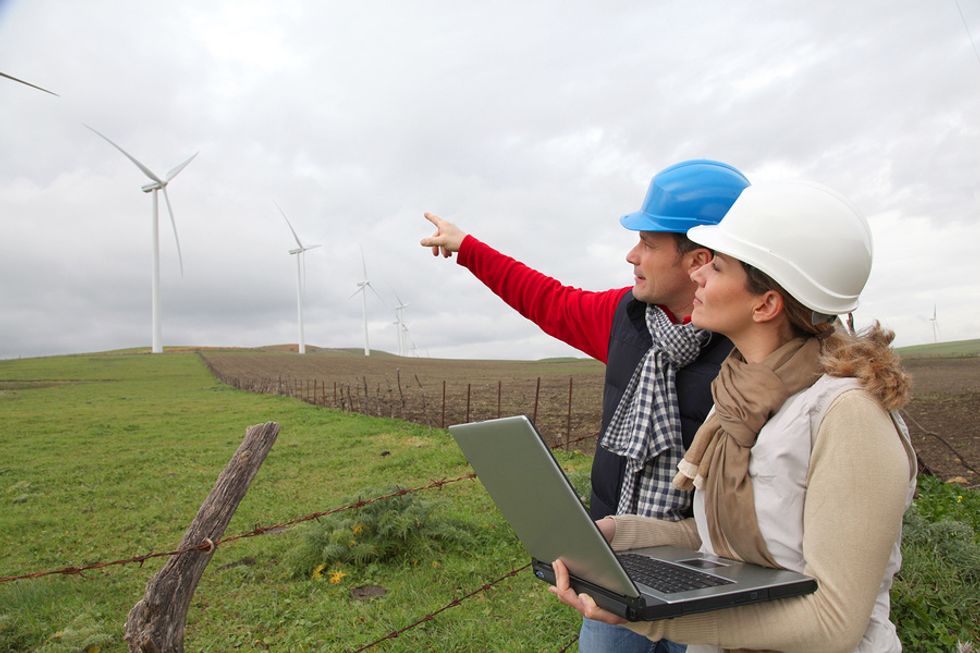 Two wind turbine service technicians researching how to fix a wind turbine outside.