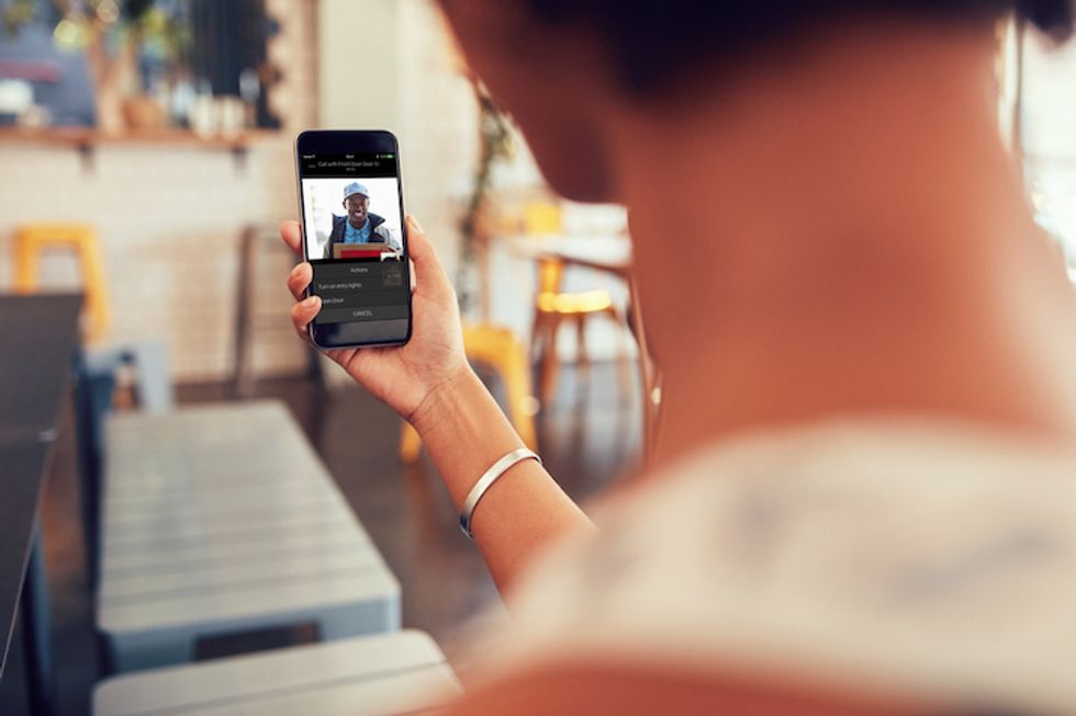 A figure holding a smartphone with a delivery person visible on the screen