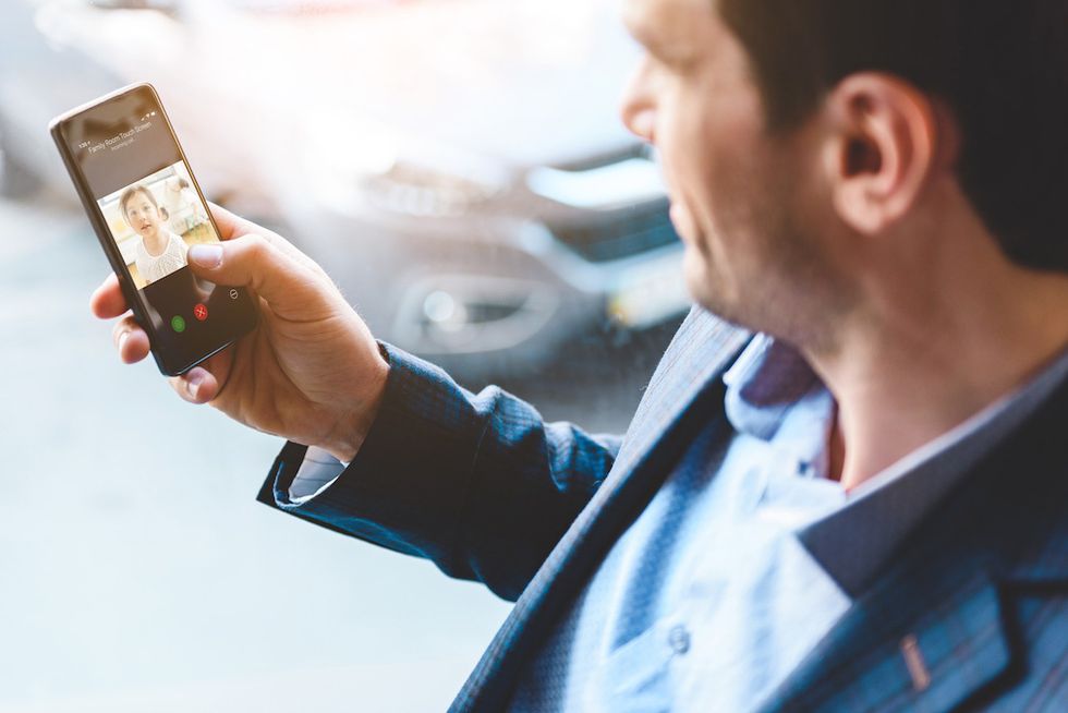 A figure holding a smartphone, looking at the screen with someone talking to them