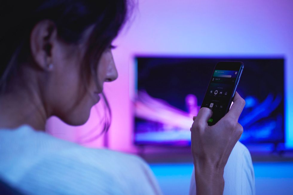 Someone holding a smartphone near a TV, operating an app