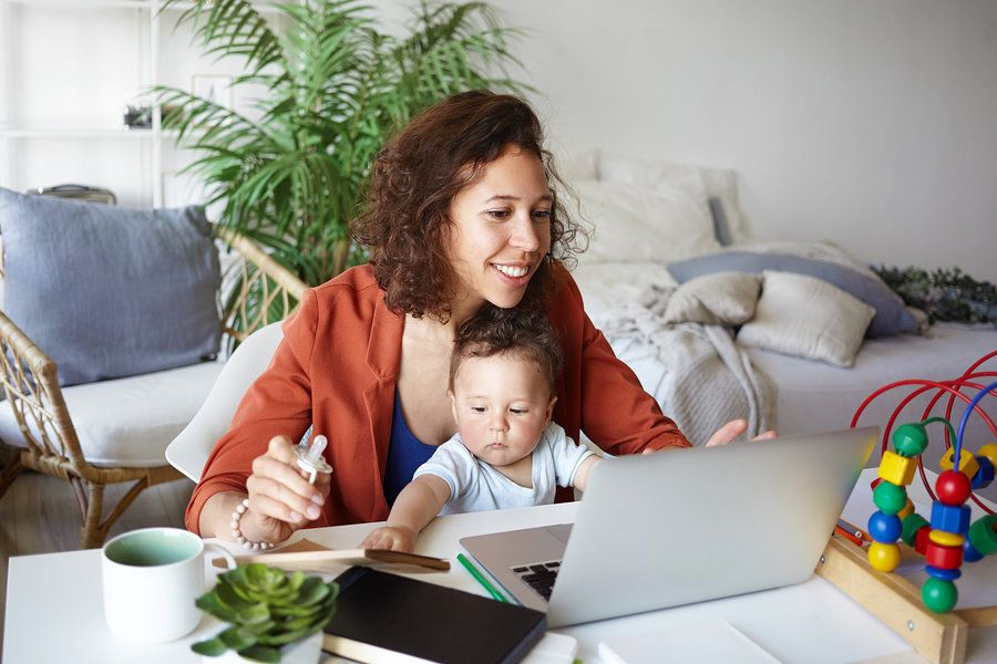 Working mom charting out her daily tasks on the computer while caring for her child.