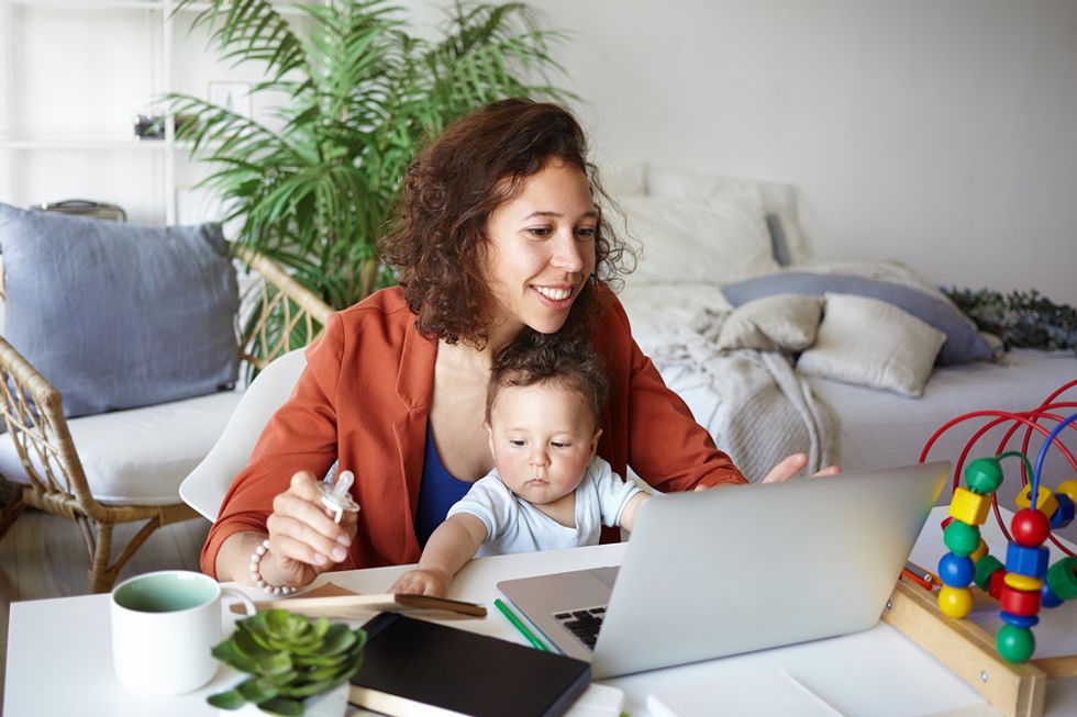 Working mom charting out her daily tasks on the computer while caring for her child.