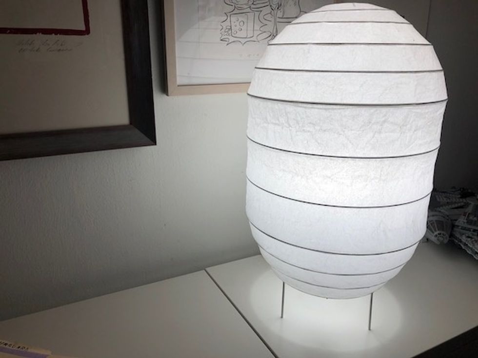 A paper lamp on a white credenza, glowing with a white light 