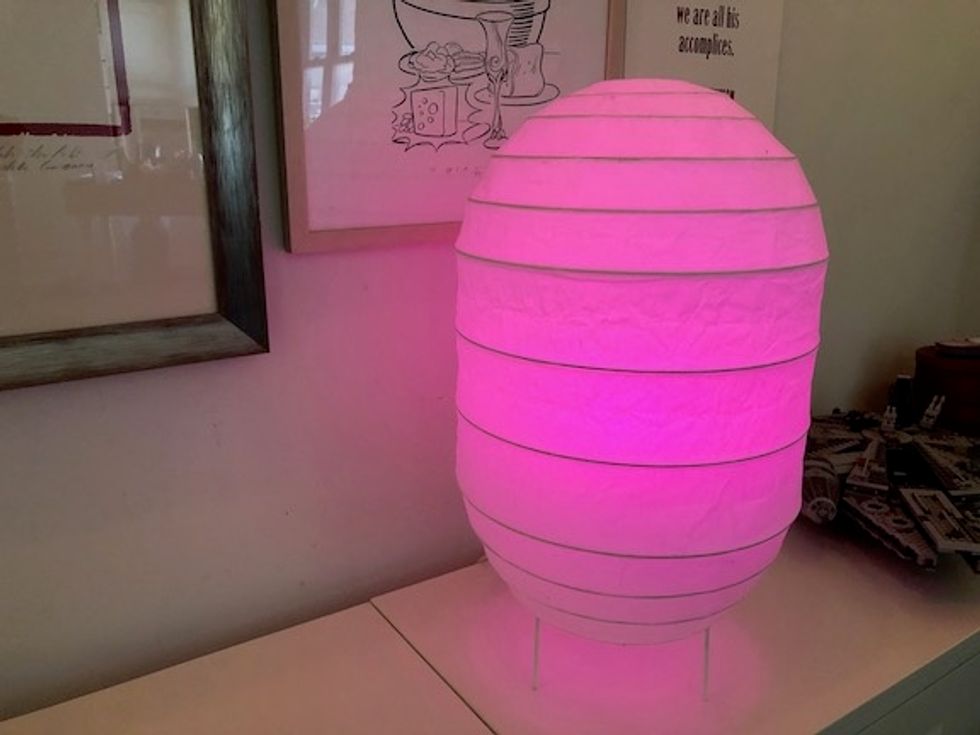 A paper lamp on a white credenza, glowing with a pink light