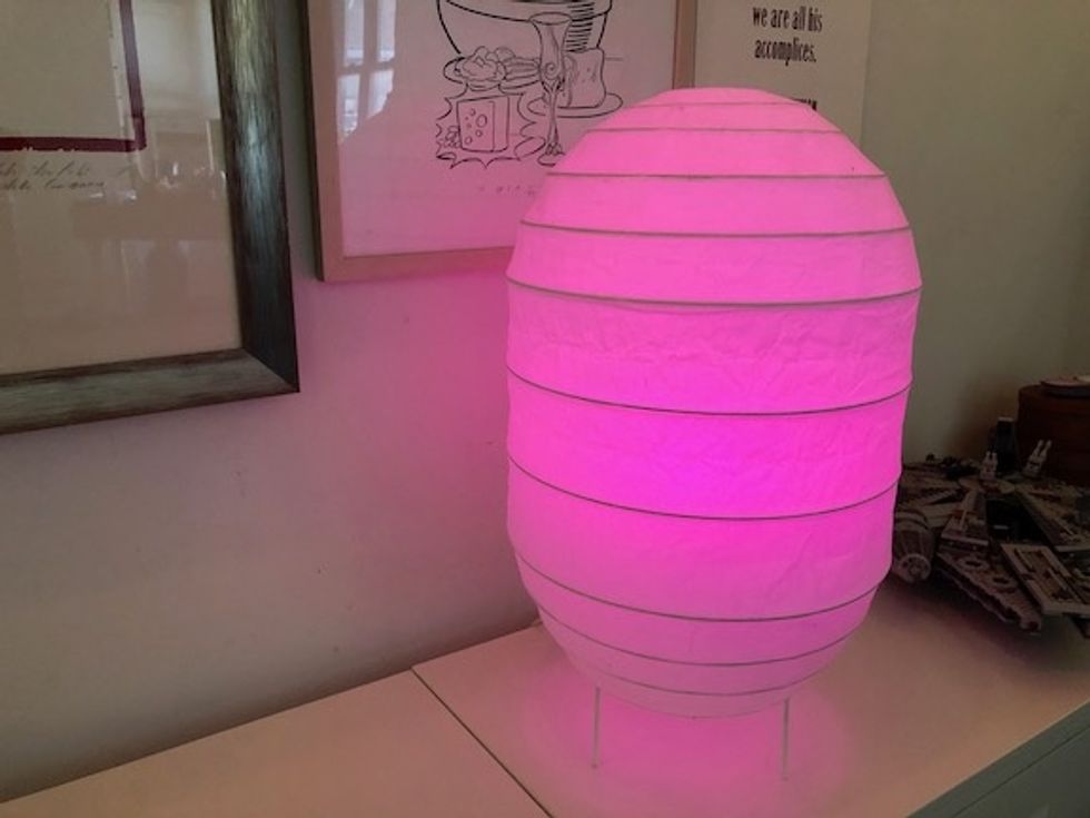 A paper lamp on a white credenza, glowing with a pink light 