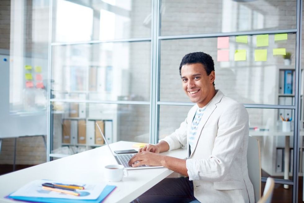 Smiling professional man working on his laptop in his office at his dream job.