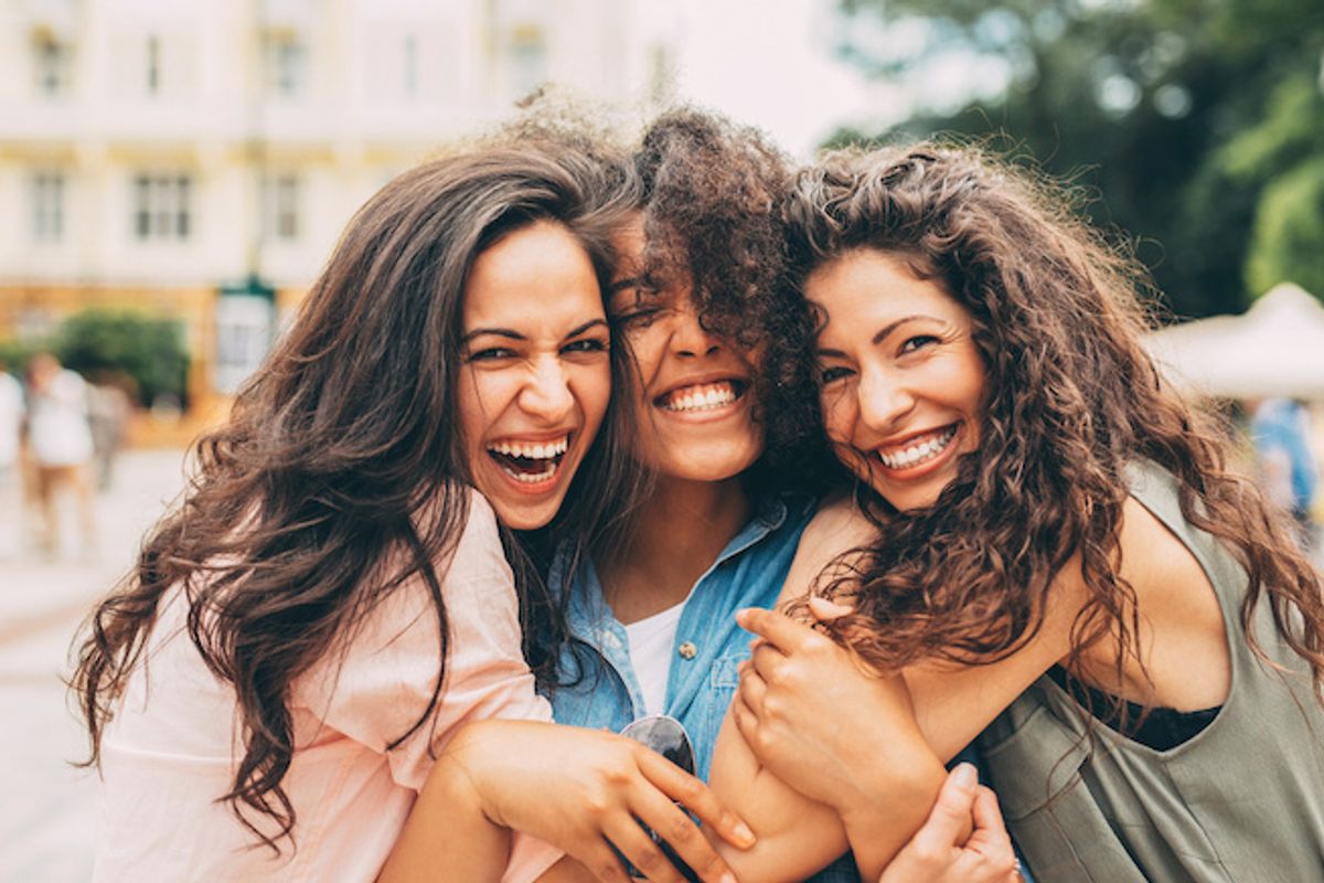 Three people with long brown curly hair smiling outside as their photo is being taken