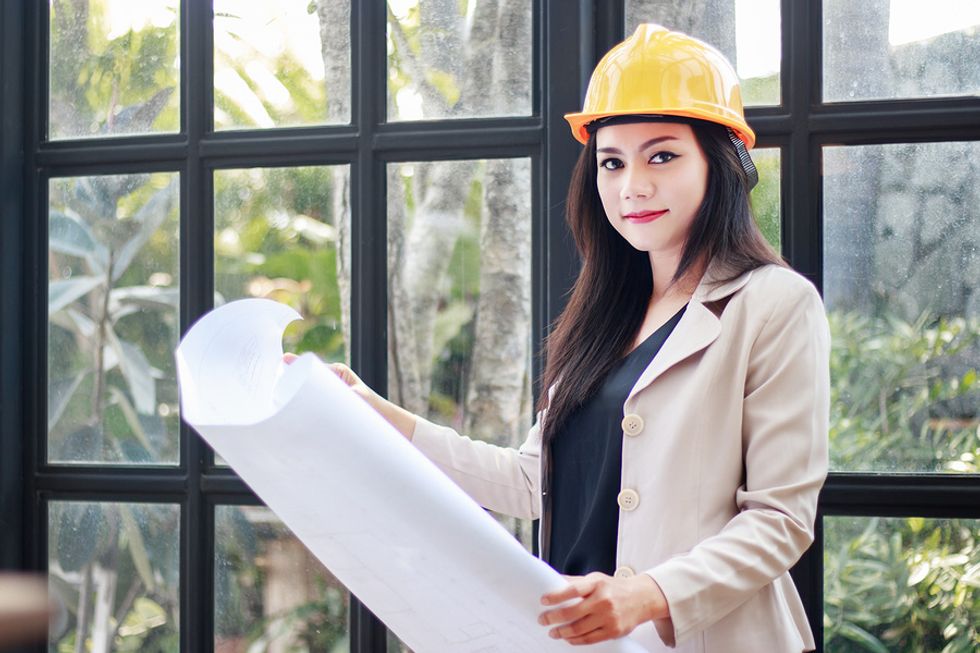 Female civil engineer wearing a hardhat and looking at blueprints while working onsite.