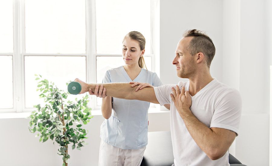 Female physical therapist helping male patient regain movement in his right arm.