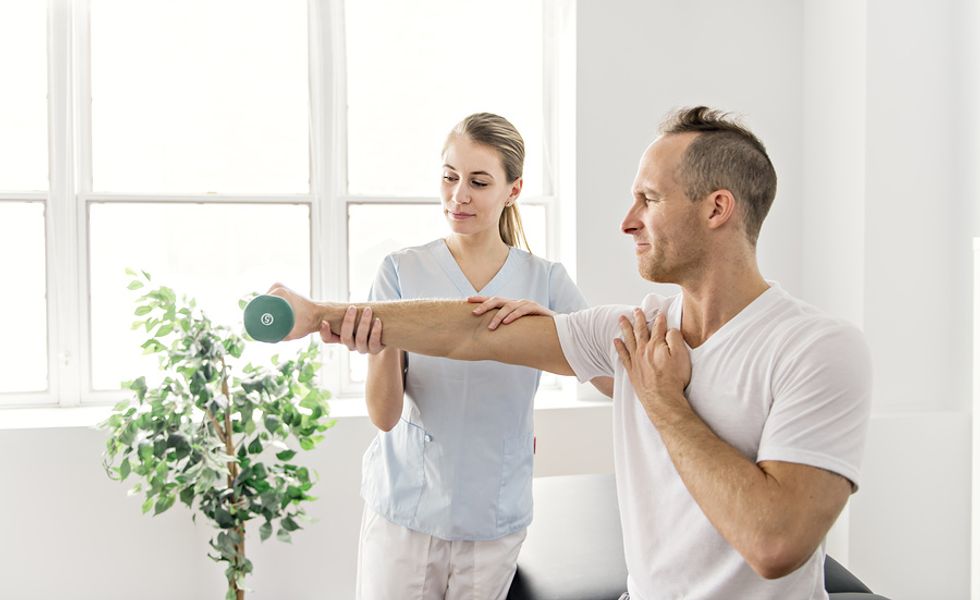 Female physical therapist helping male patient regain movement in his right arm.