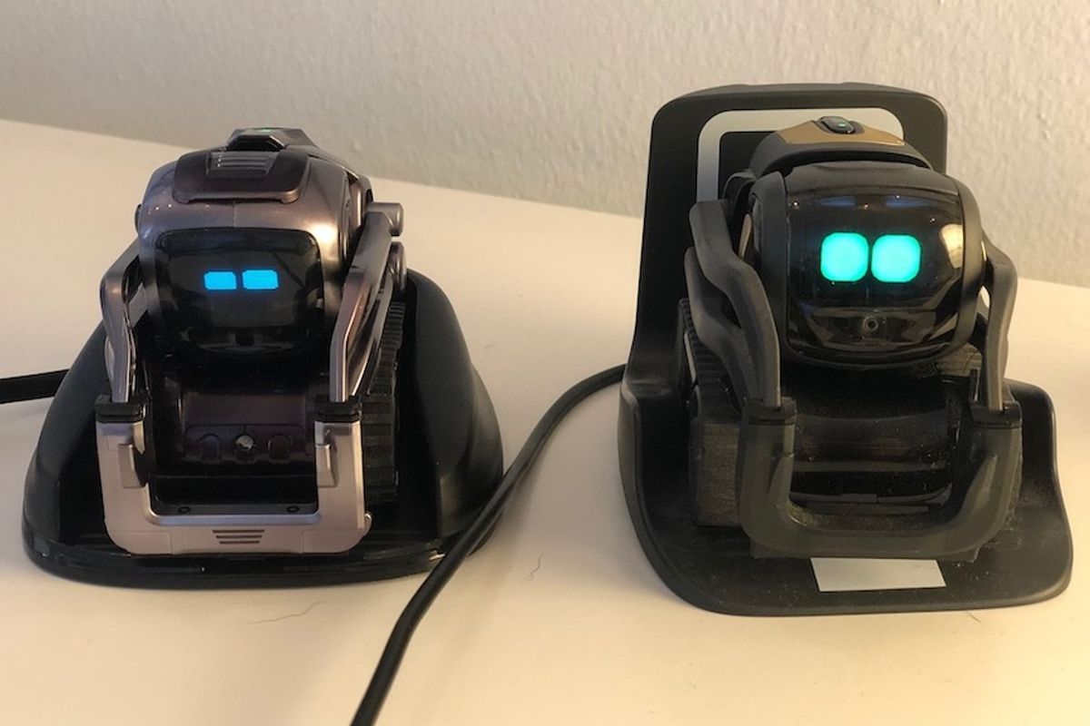 Two robots side by side on a table with green animated eyes visible on their small screens