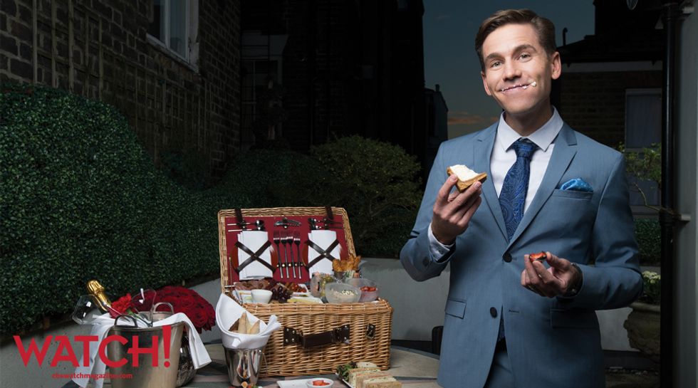 Brian Dietzen in a blue grey suit and smiling with a mouthful of cheese