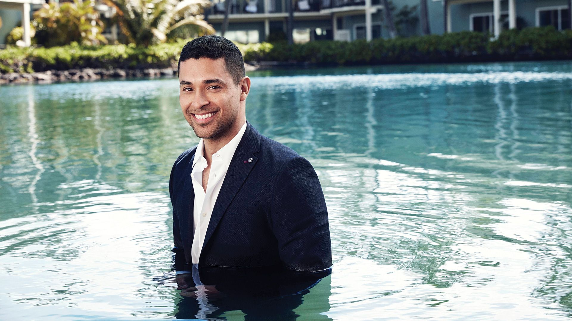 Wilmer Valderrama descends fully dressed in a jacket and shirt into a swimming pool.