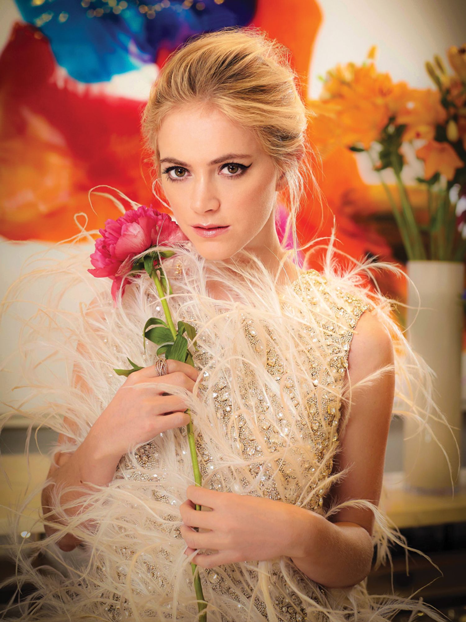 Emily Wickersham in a plumed and sequined dress holding a flower.