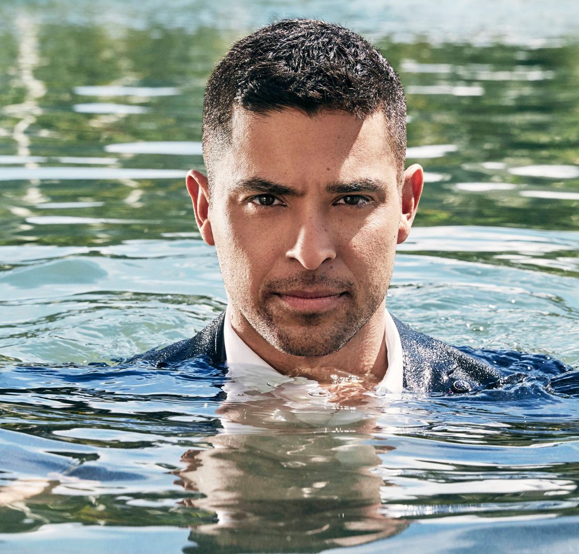 Wilmer Valderrama rises fully dressed from a swimming pool.