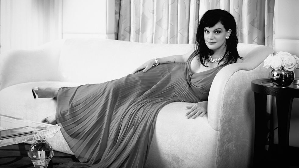 Black and white image of Actress Pauley Perrete reclining on a couch in a pleated dress.