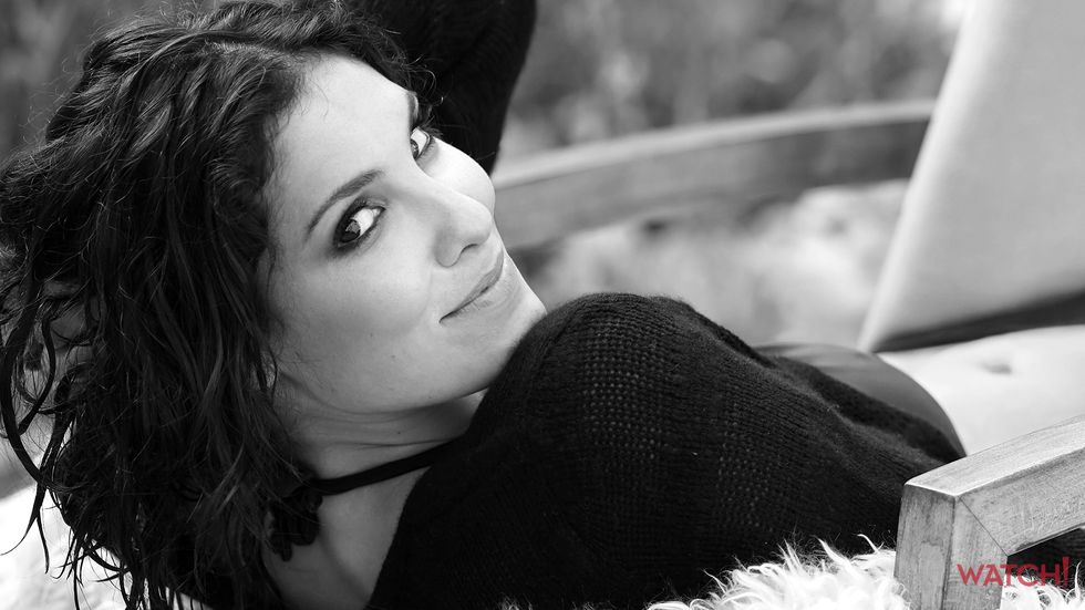 Daniela Ruah of NCIS Los Angeles with curly hair smiling over her shoulder