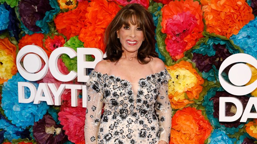 Kate Linder standing infront of a floral background containing CBS Daytime logo