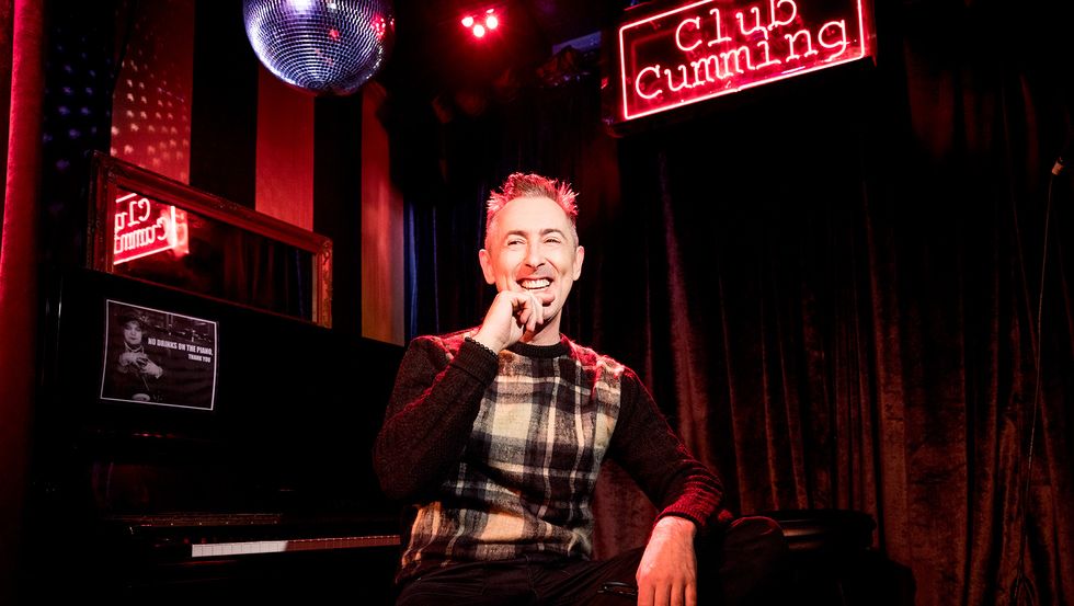 Alan Cumming of Instinct in plaid sweater under disco ball at Club Cumming