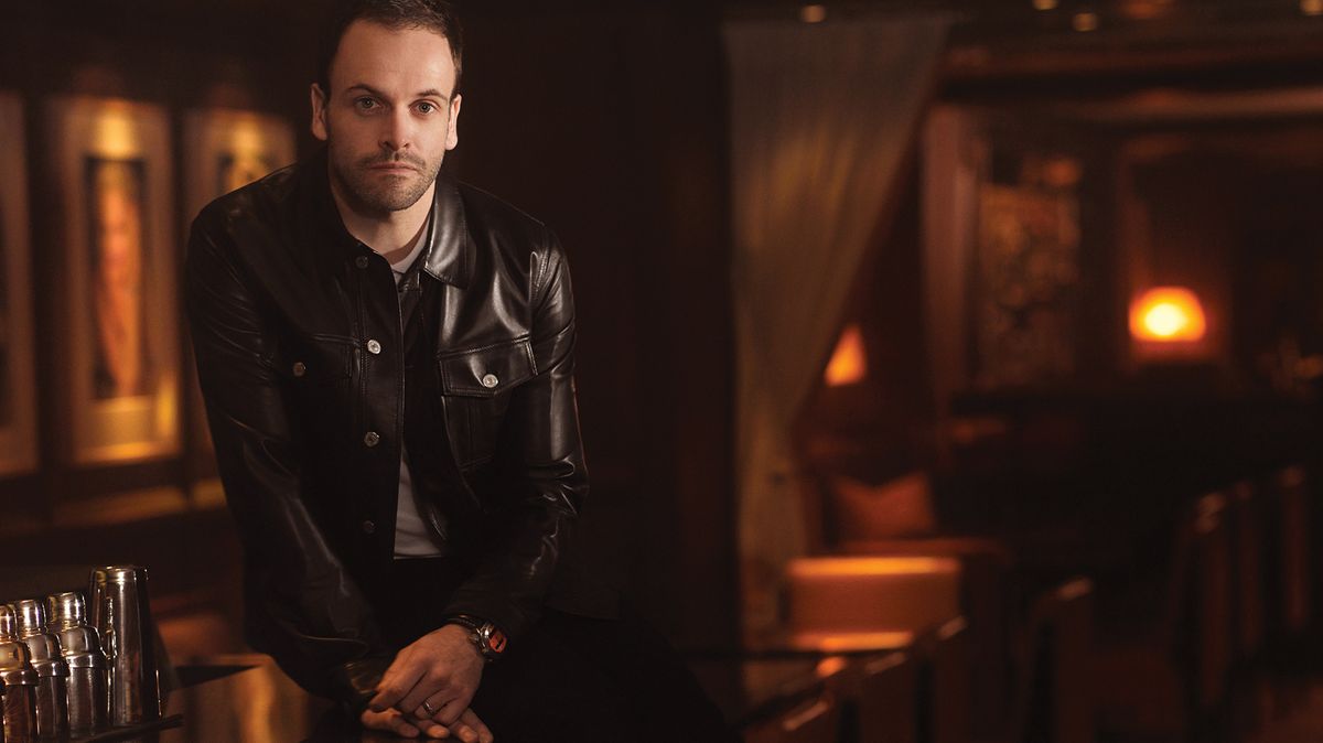 Jonny Lee Miller of Elementary in leather jacket posing at bar
