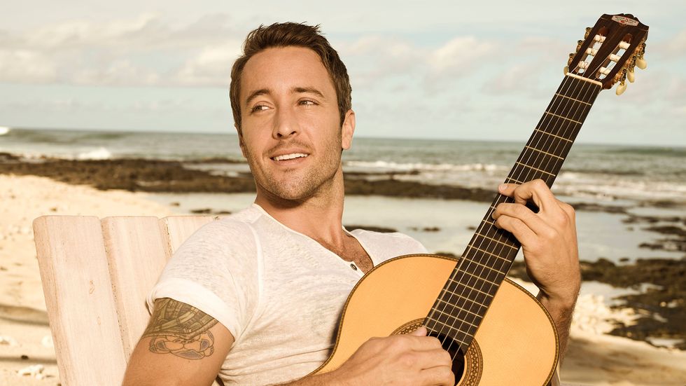 Alex OLaughlin of Hawaii Five 0 on beach playing guitar