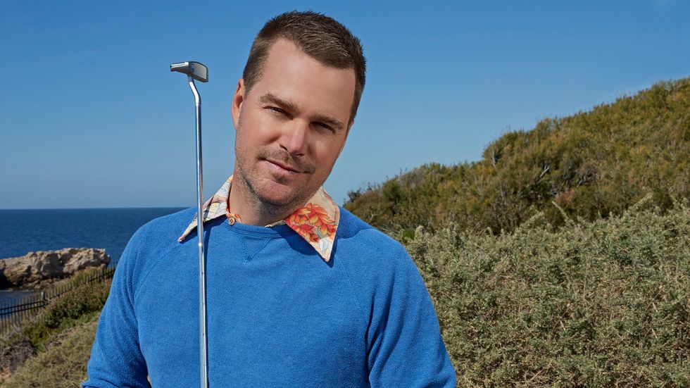 Chris O'Donnell wears a blue sweatshirt with a flowered collar while standing on a golf course.
