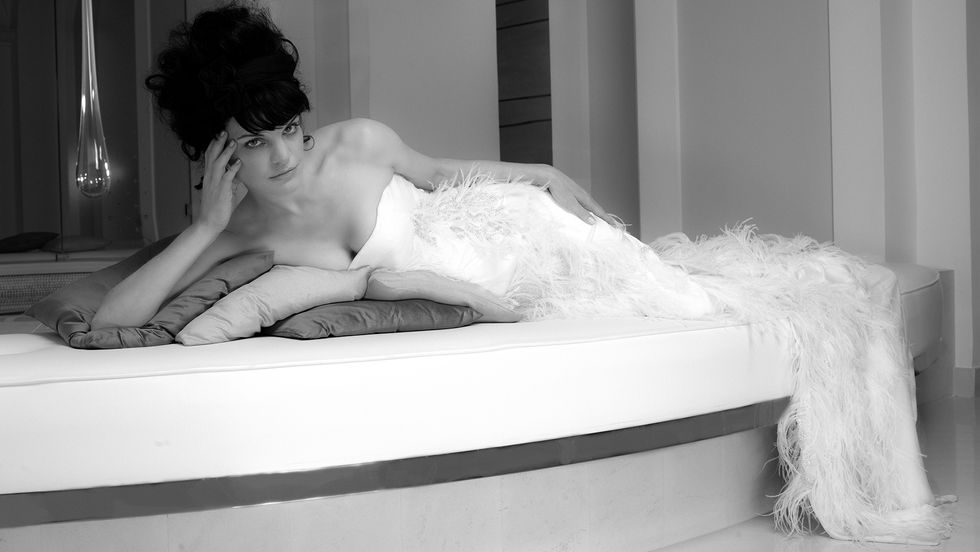 Black and white image of Actress Pauley Perrete reclining in a feathered dress.