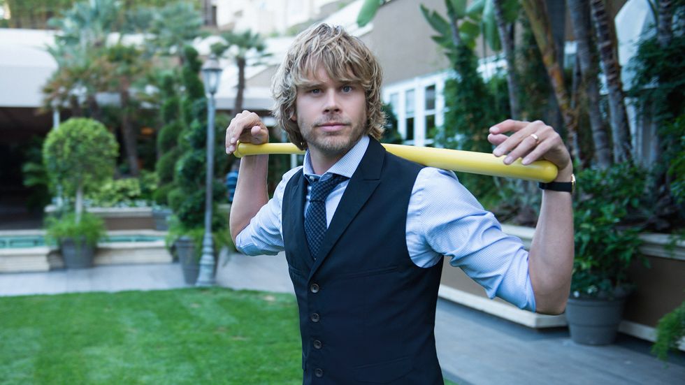 Eric Christian Olsen wearing a vest and resting his arms on a wiffle bat