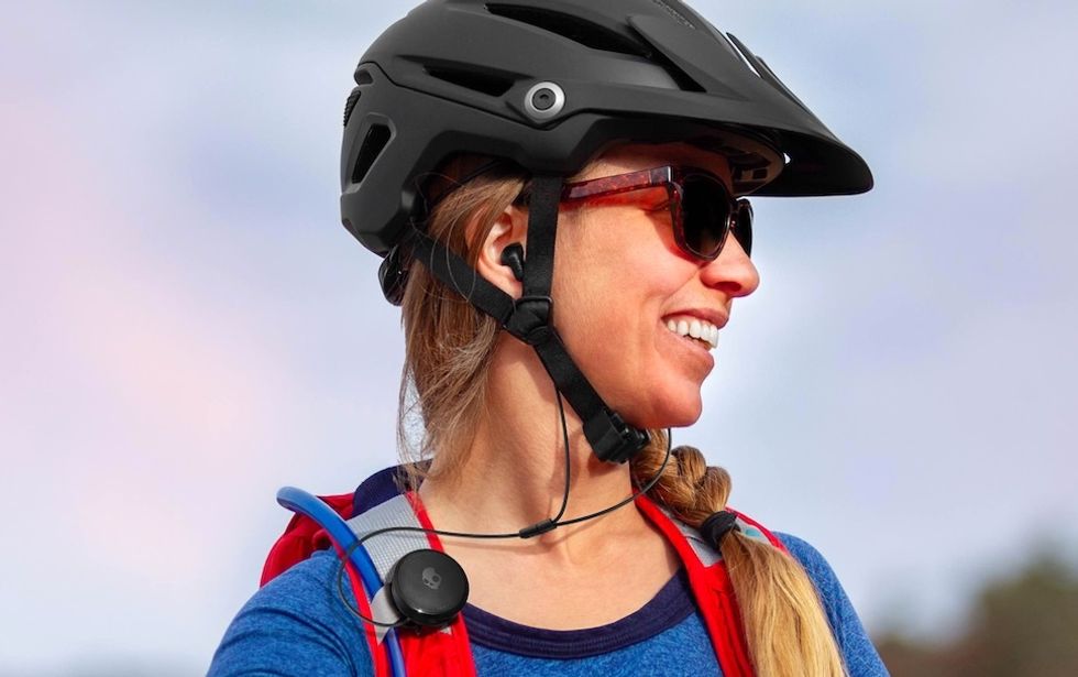 Someone wearing Skullcandy Vert earbuds clipped to a backpack