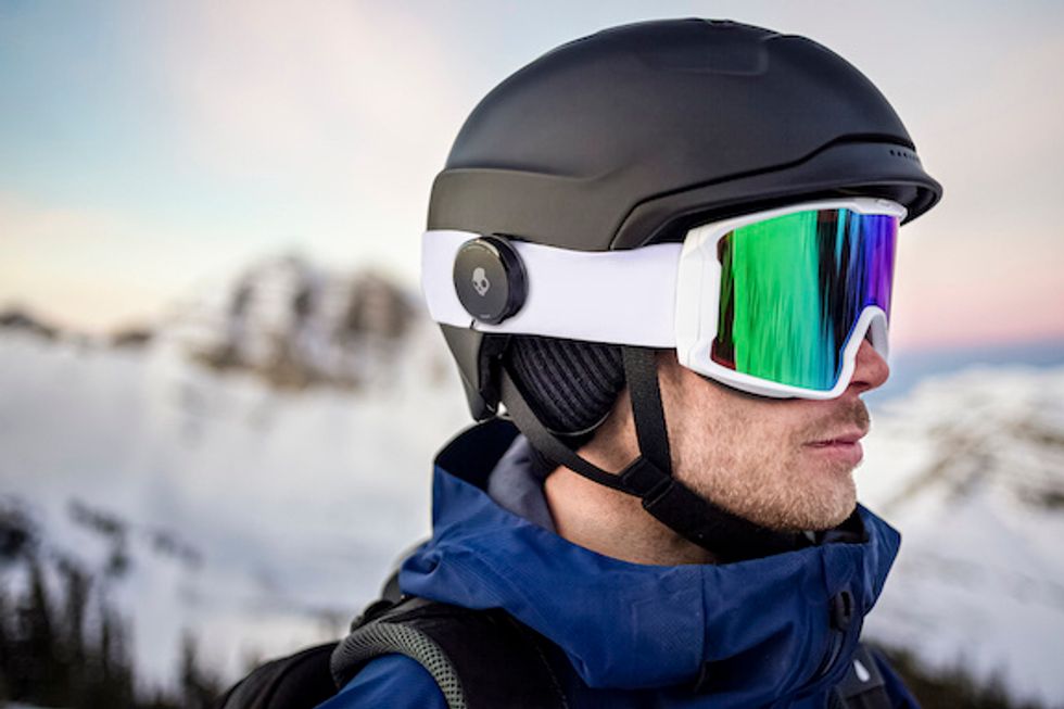 A man wearing snow goggles and a black helmet in the snow with Skullcandy Vert earbuds