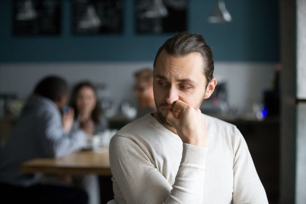 Introverted young man sitting separate from his co-workers in a break room.