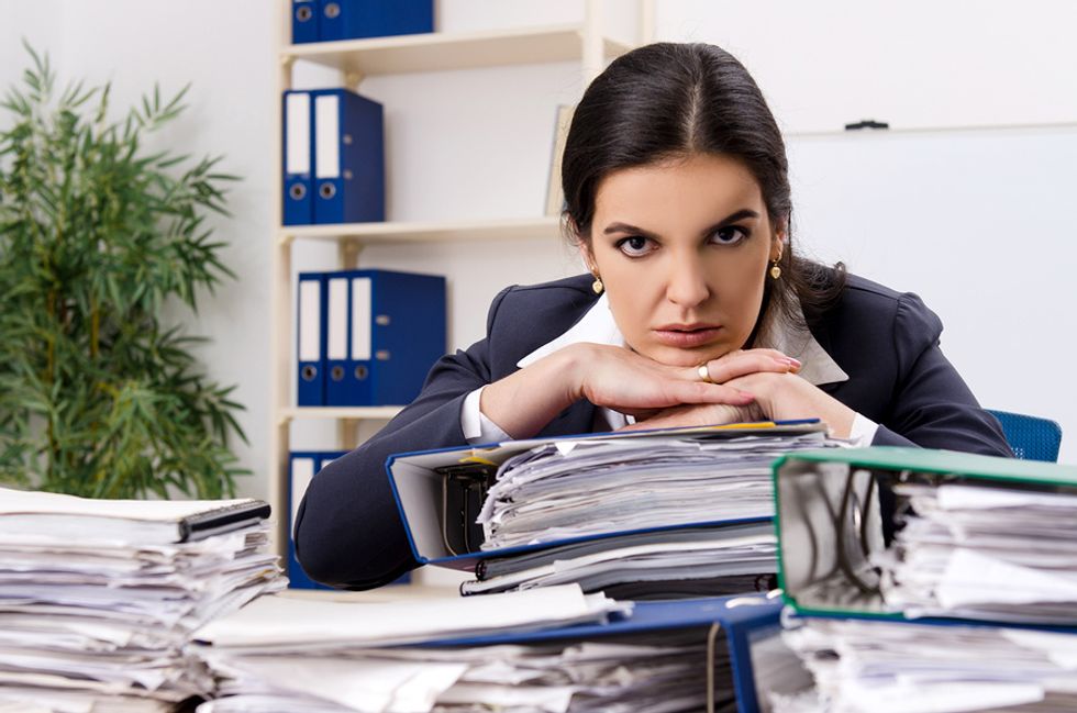 Female employee looking unhappy with the work she has at her desk and deciding whether she should find a new job.