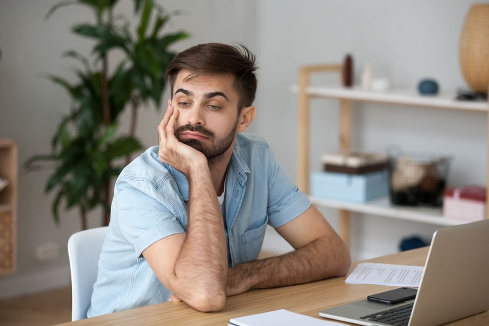 Young man looking bored at his desk and deciding whether he should get another job.