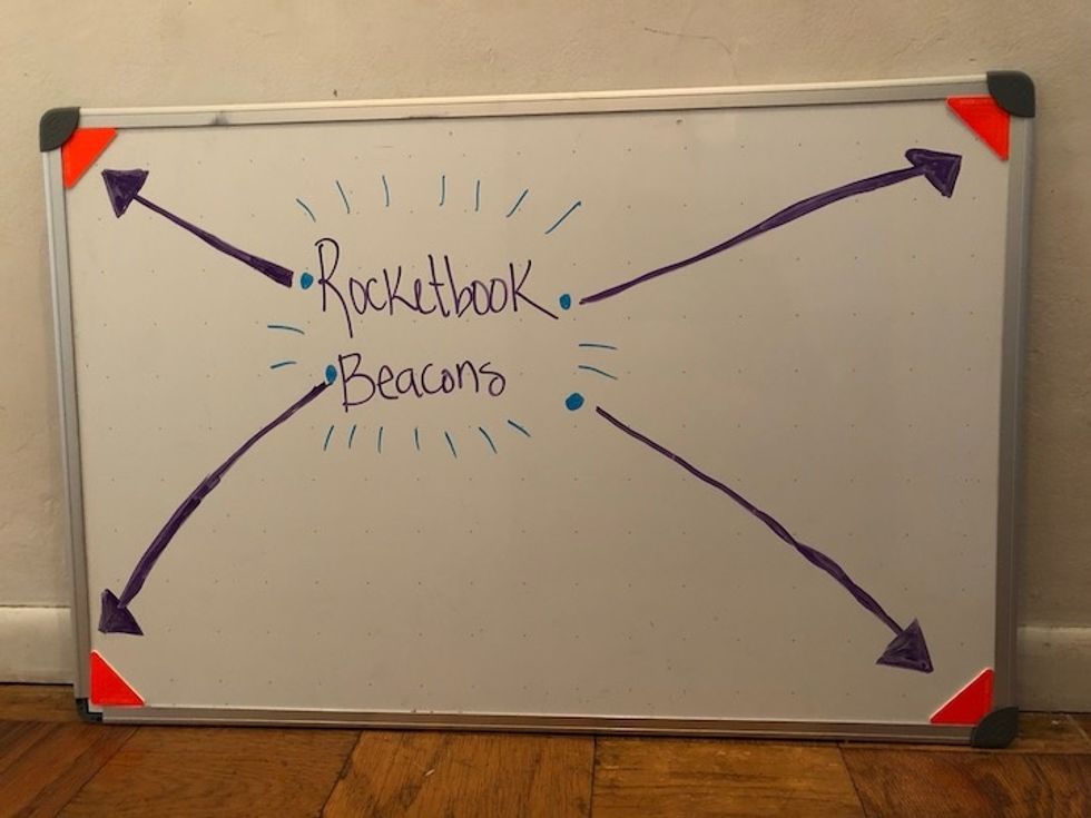 A whiteboard with four orange Rocketbook Beacons in the corners