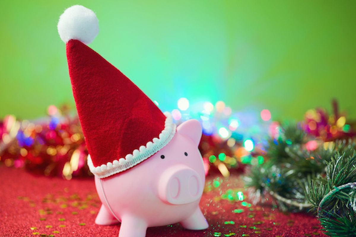 A pink piggy bank with a red Santa hat, with holiday decorations and green trees behind