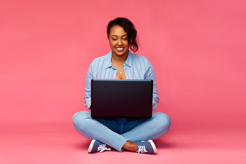 Happy woman on her laptop using Work It Daily's free cover letter samples to write her own great cover letter.