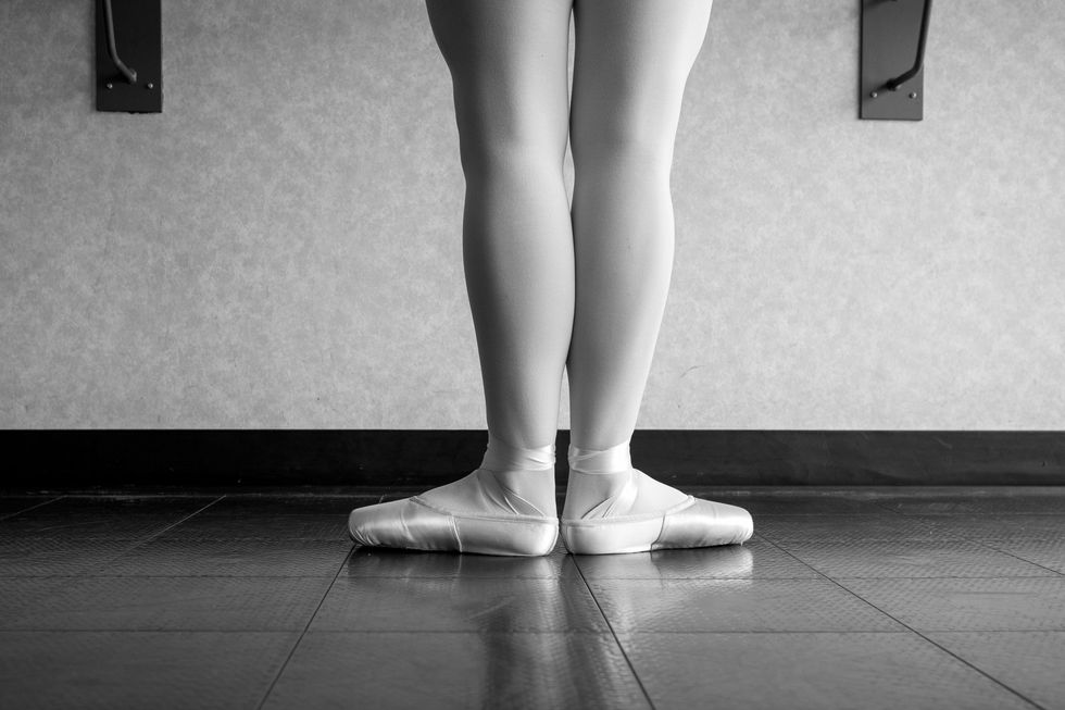 Black and white version of back view of ballet dancer ballerina at the barre in dance class standing in first position