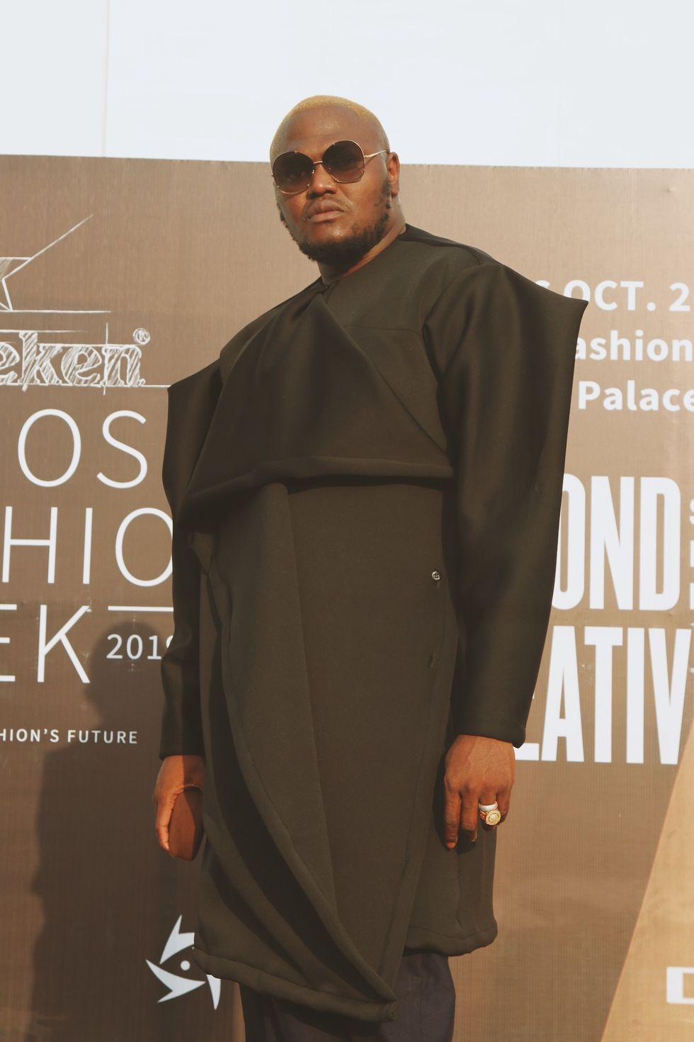 Tall Nigerian man wearing a structural black coat and big sunglasses at Lagos Fashion Week 2019