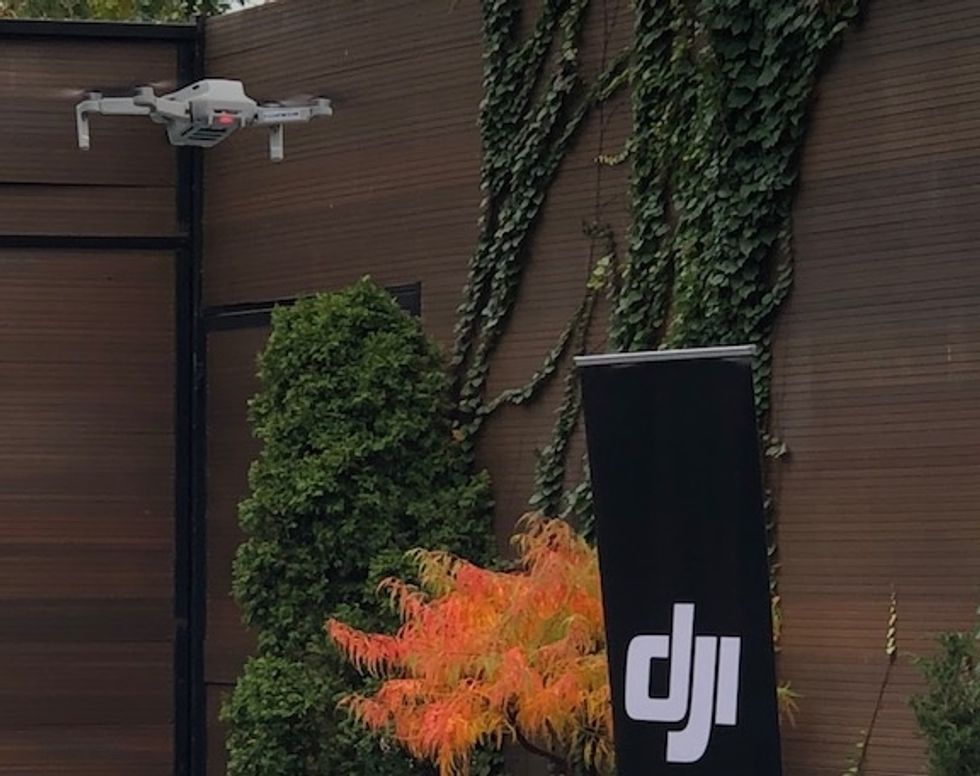 The DJI Mavic Mini in mid-air outside next to a DJI logo