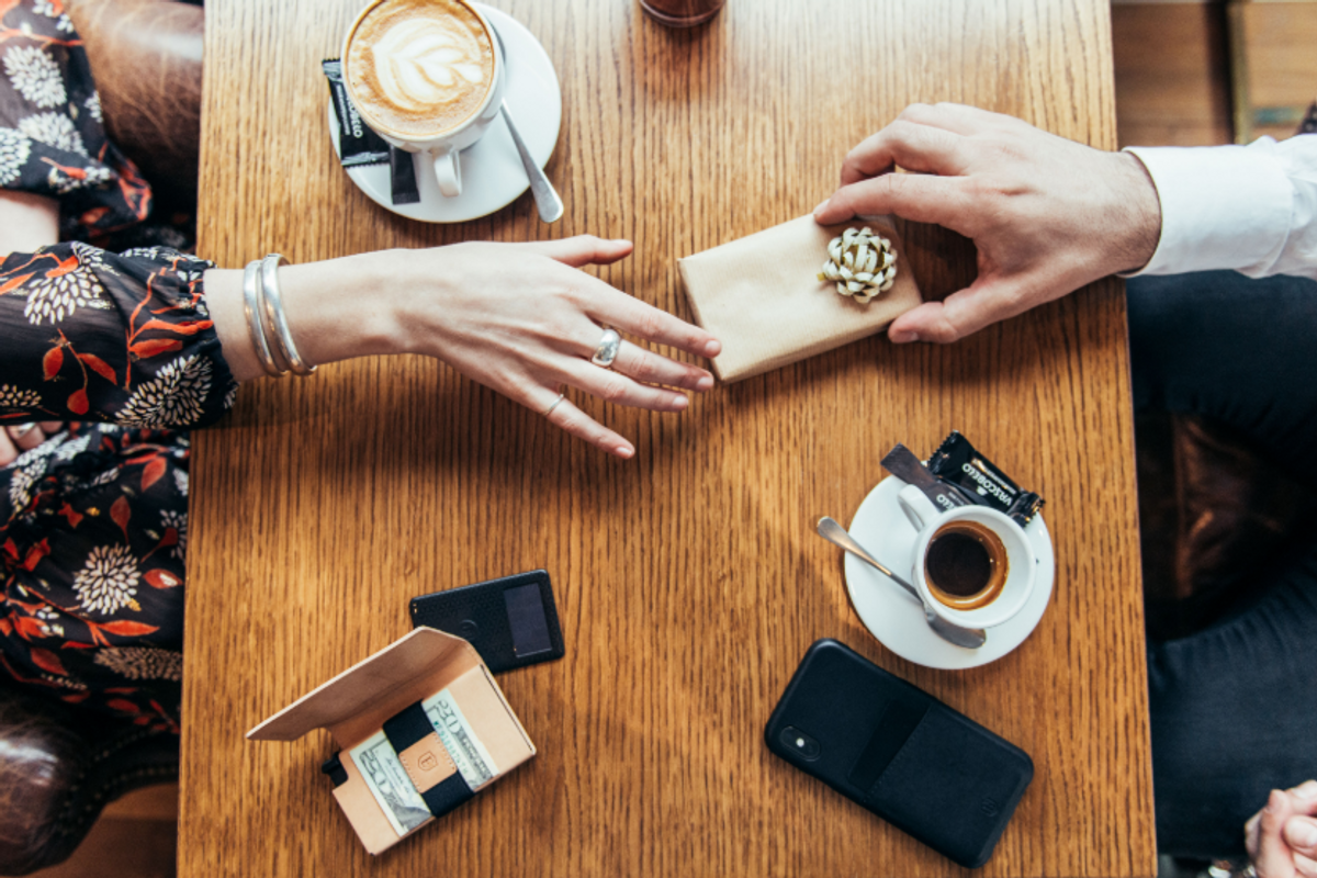 On a wooden table with an Ekster wallet, a man gives a woman wearing a ring a small gift