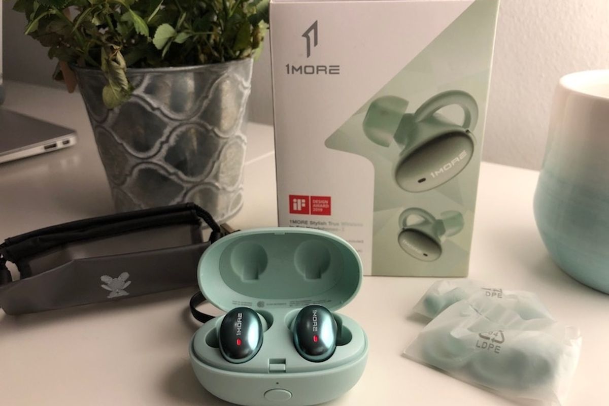 A pair of mint green 1More Stylish True Wireless In-Ear Headphones in the matching green case on a white table