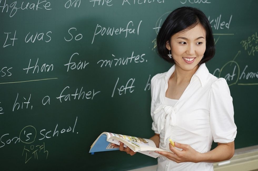 Young woman in front of a chalkboard teaching English overseas.