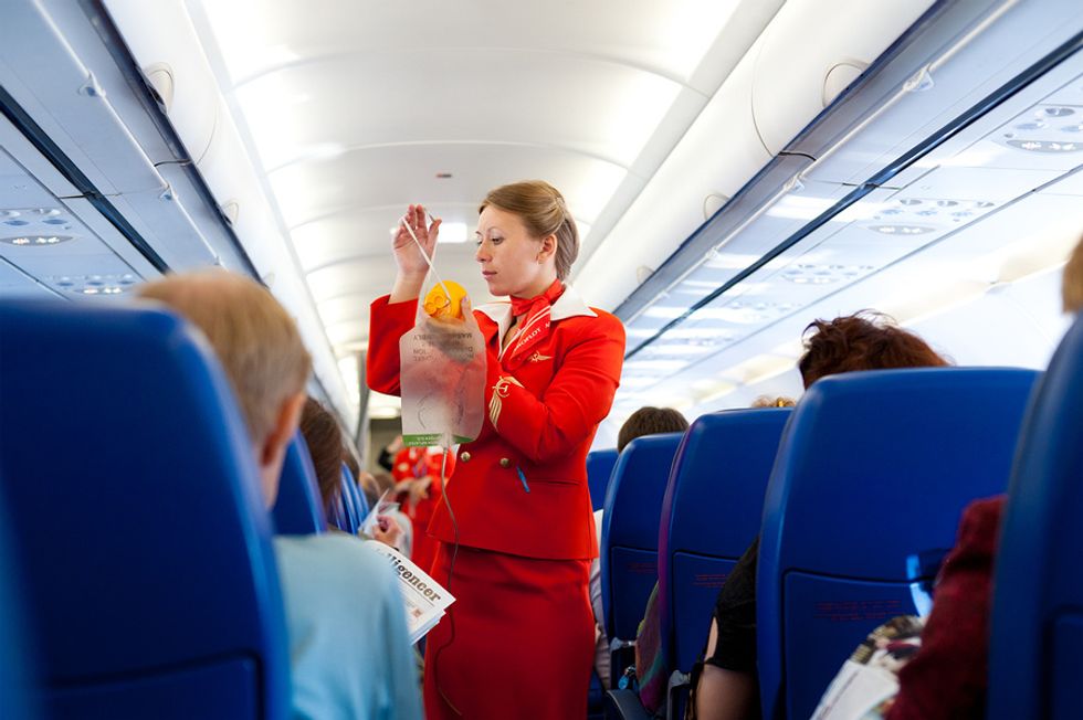 Female flight attendant showing passengers how to use their oxygen masks on an airplane.