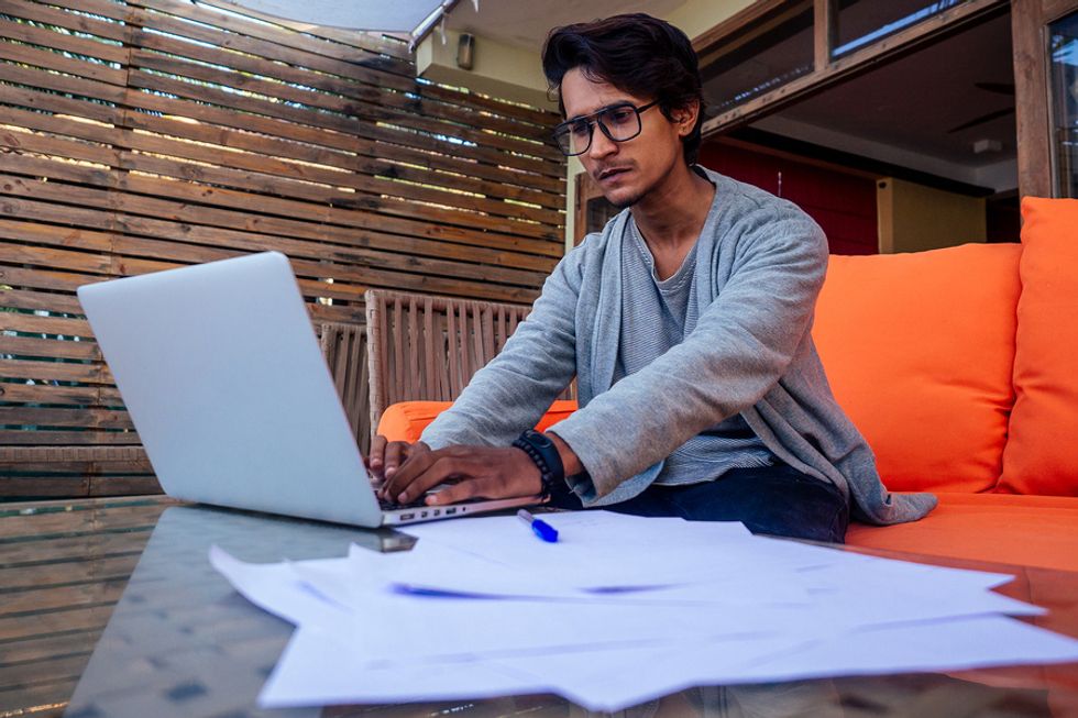 Young man sitting on a couch and working on his laptop as he freelances overseas.